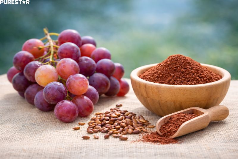 Fresh grapes, grape seeds, and reddish-brown grape seed extract powder displayed together as a natural antioxidant source.